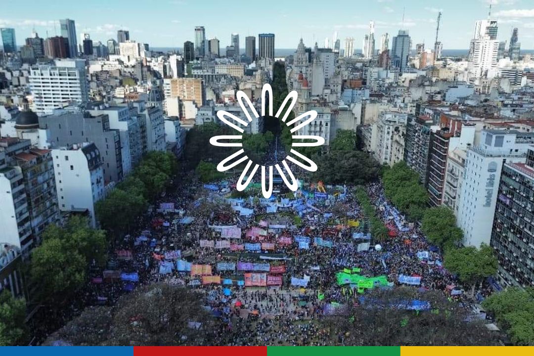 Logo de Augm en blanco. imagen aerea de concentración universitaria en defensa del Financiamiento Universitario, Argentina.